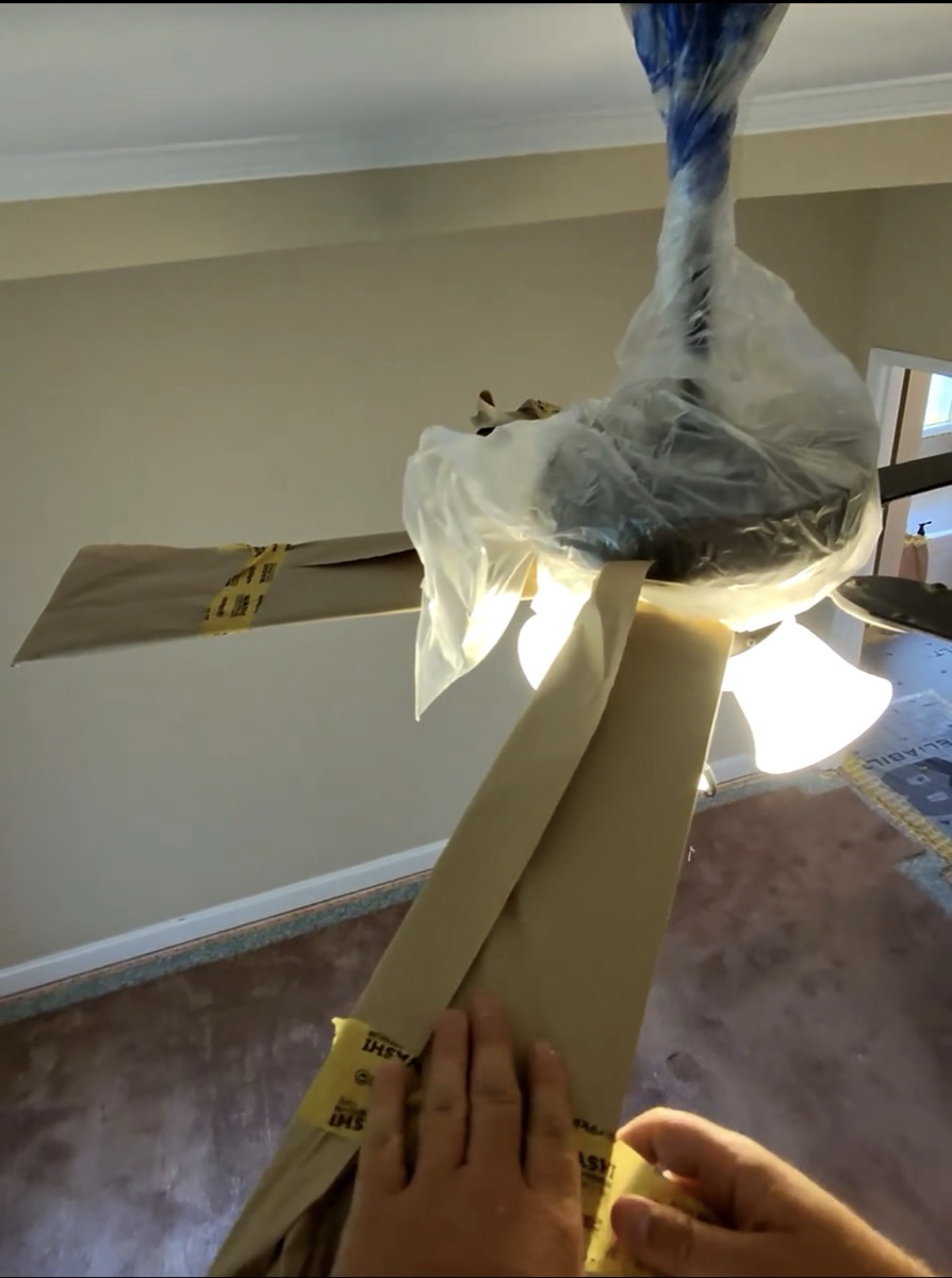 Ceiling fan fully masked for spraying with paper-wrapped blades secured by Washi painter's tape and a plastic-bagged motor